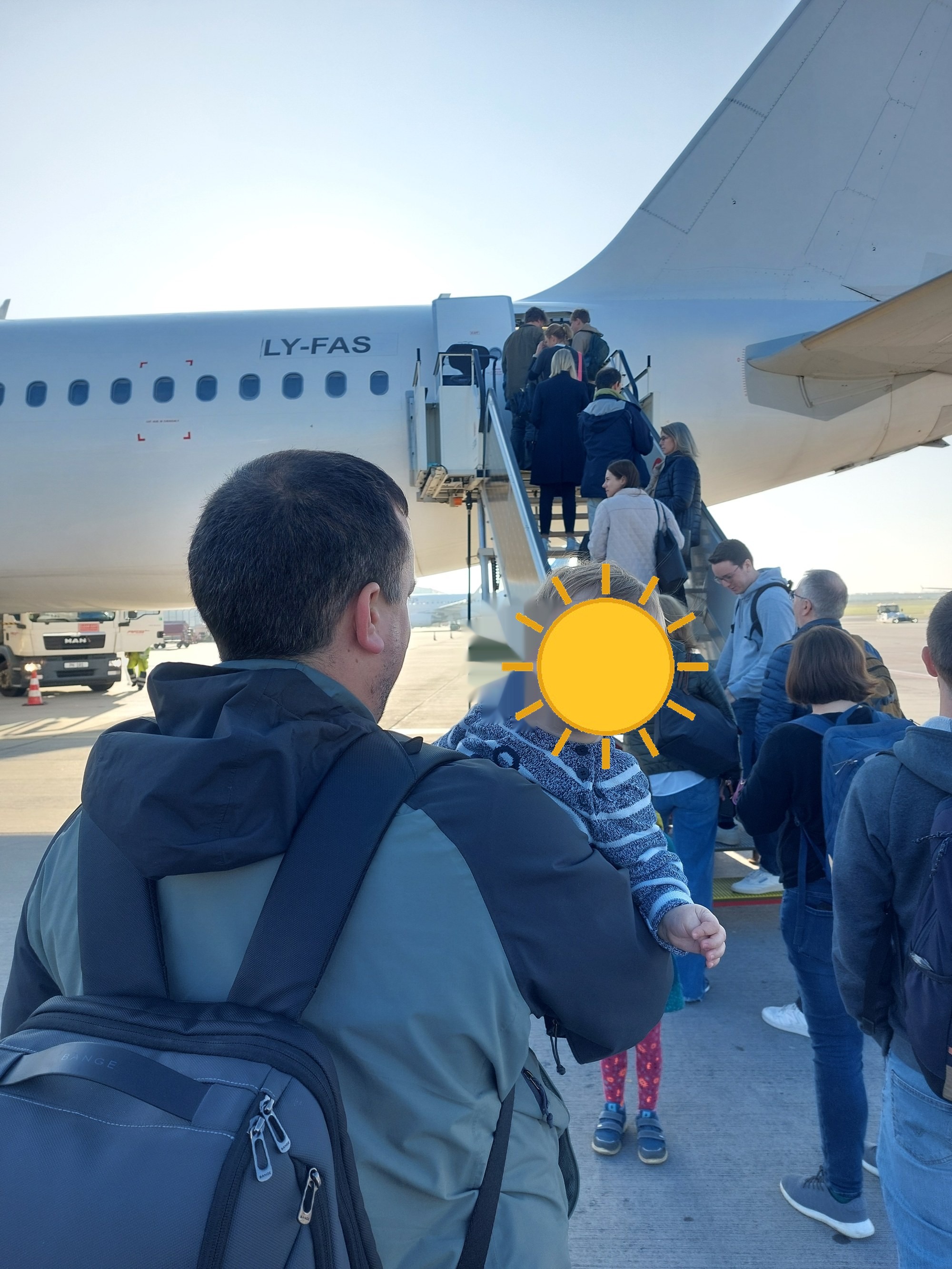 Lolo auf Papas Rücken beim Boarding, im Hintergrund das Flugzeug (Gesicht mit Sonne verdeckt)