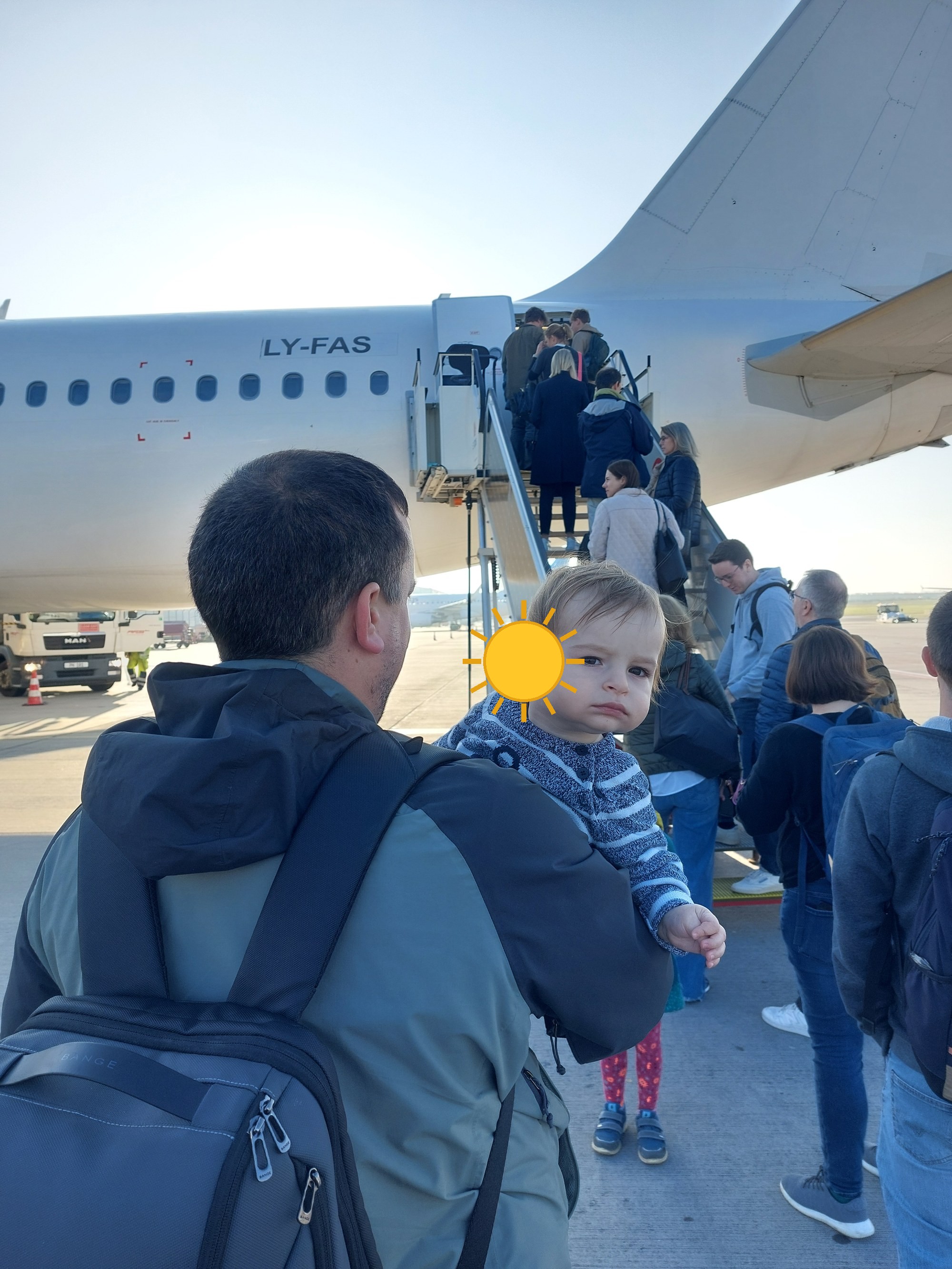 Lolo auf Papas Rücken beim Boarding, im Hintergrund das Flugzeug (Gesicht mit Sonne verdeckt)