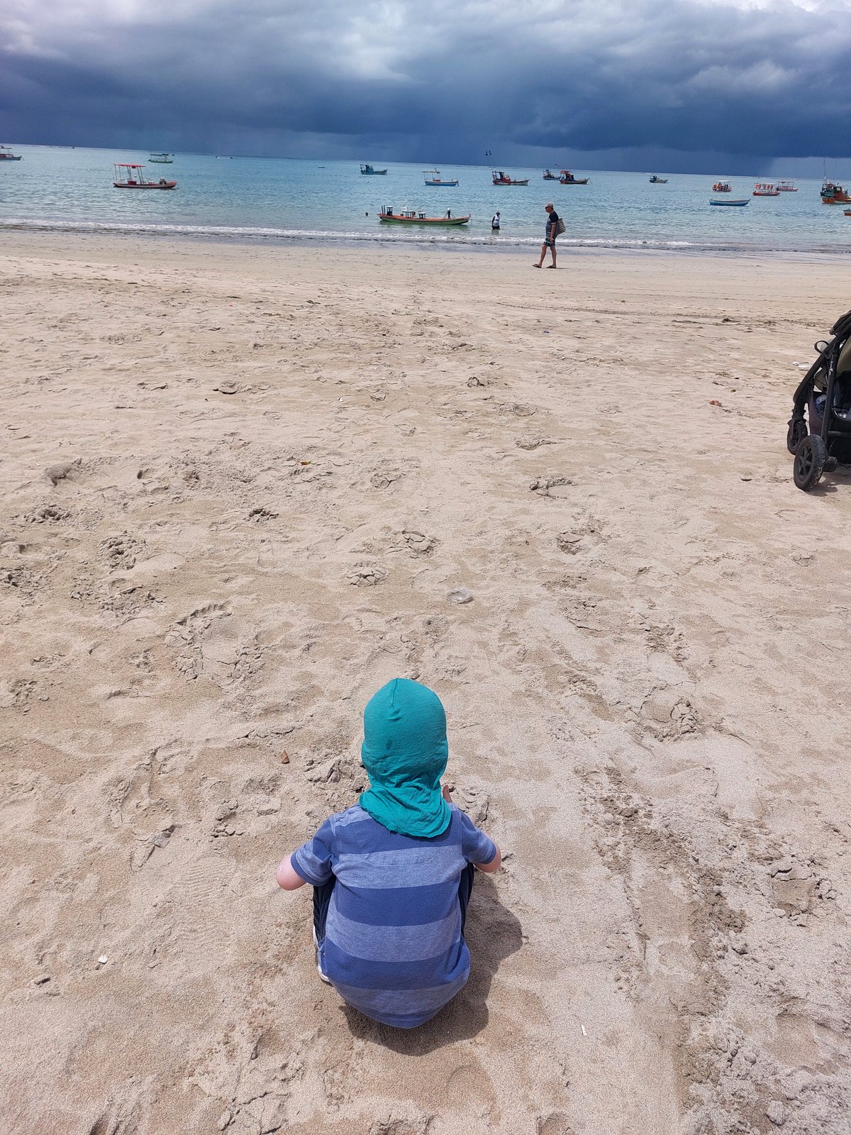 Lolo sitzt am Strand von Maceió bei aufziehendem Gewitterhimmel (von hinten)